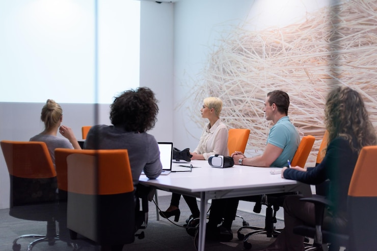 A small group seated at a meeting table with orange chairs